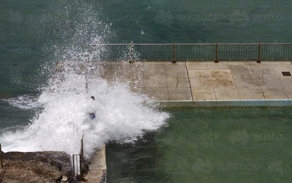 Person standing in wave crashing over rocks into rock pool - Australian Stock Image