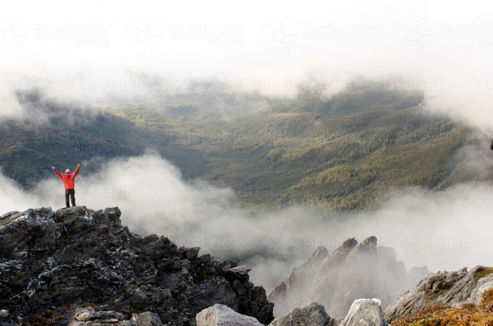 Person standing on a cliff in a misty mountain range - Australian Stock Image