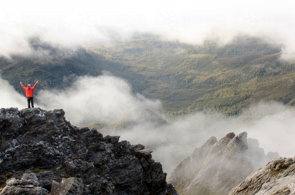 Person standing on a cliff in a misty mountain range - Australian Stock Image