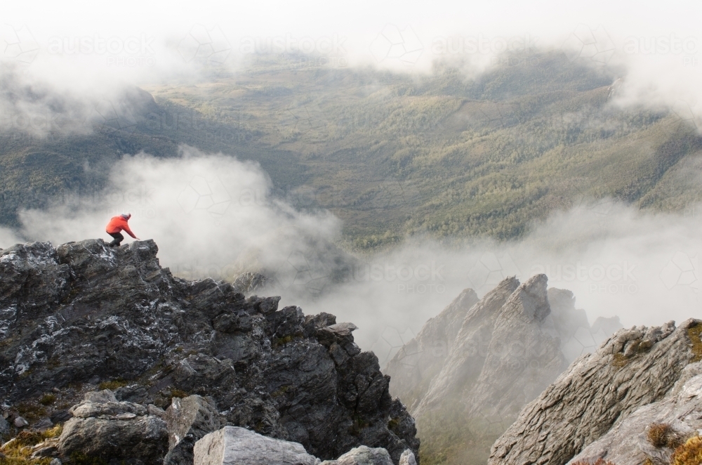 Person standing on a cliff in a misty mountain range - Australian Stock Image
