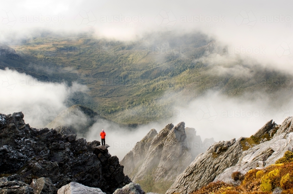 Person standing on a cliff in a misty mountain range - Australian Stock Image