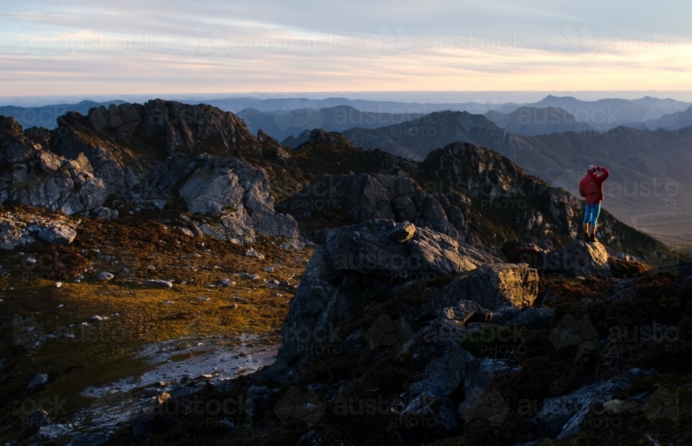 Person standing on cliff, looking out over mountain range - Australian Stock Image