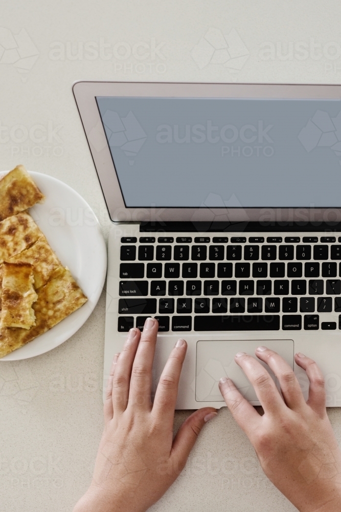 person typing on a laptop with grilled cheese snack - Australian Stock Image