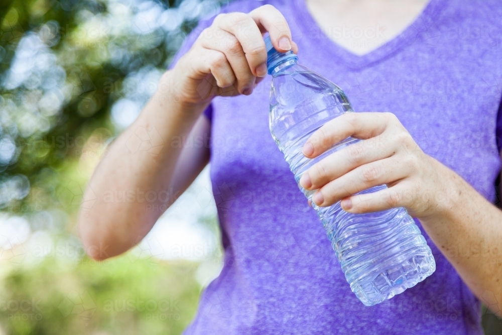 Person uncapping plastic water bottle - Australian Stock Image
