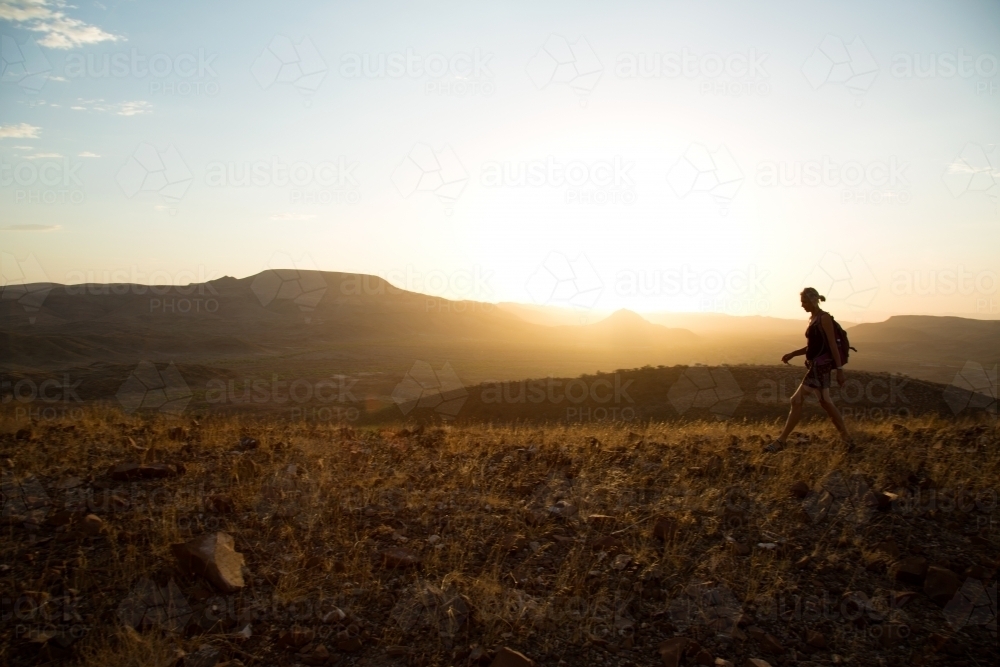 Person walking across hills at sunrise - Australian Stock Image