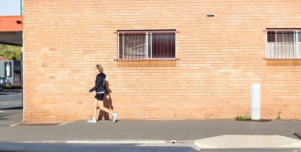 Person walking along footpath in front of brick building - Australian Stock Image
