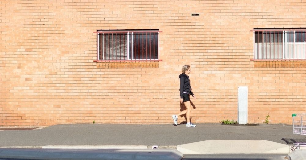 Person walking along footpath in front of brick building - Australian Stock Image