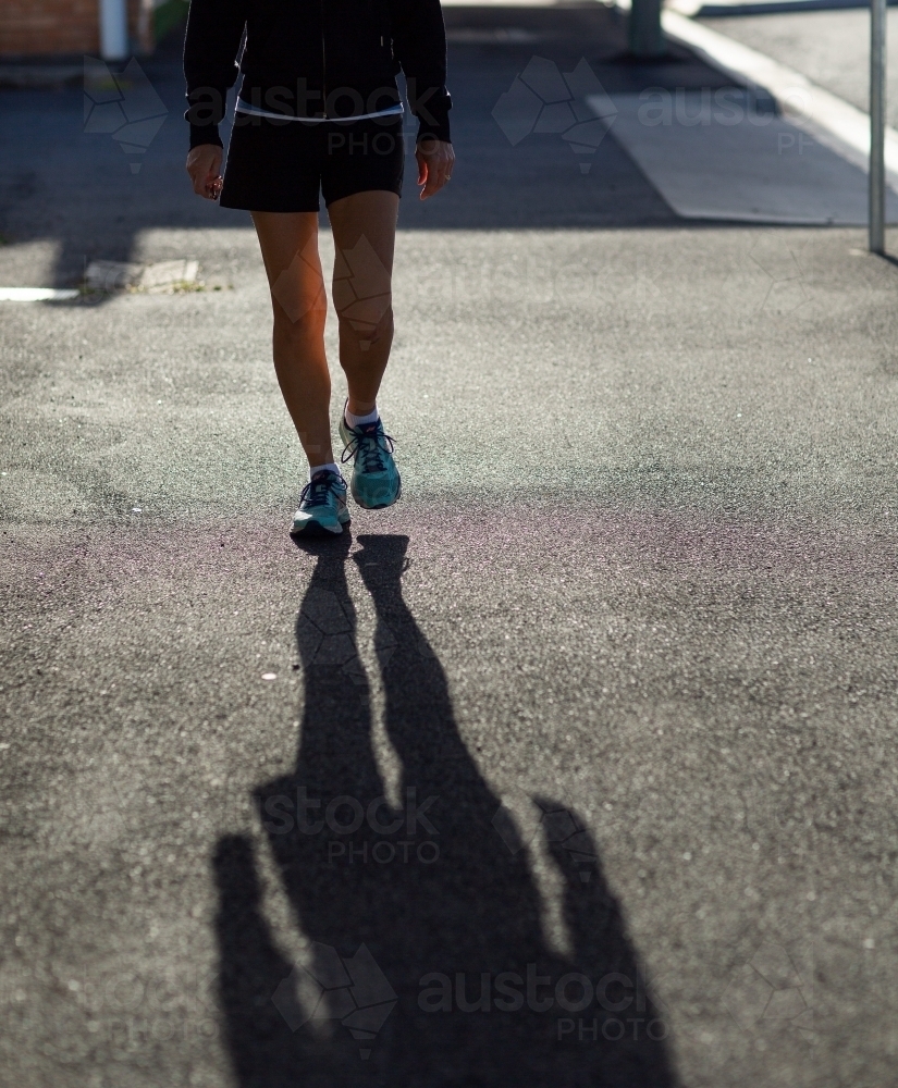 Person walking from waist down with long shadow in foreground - Australian Stock Image