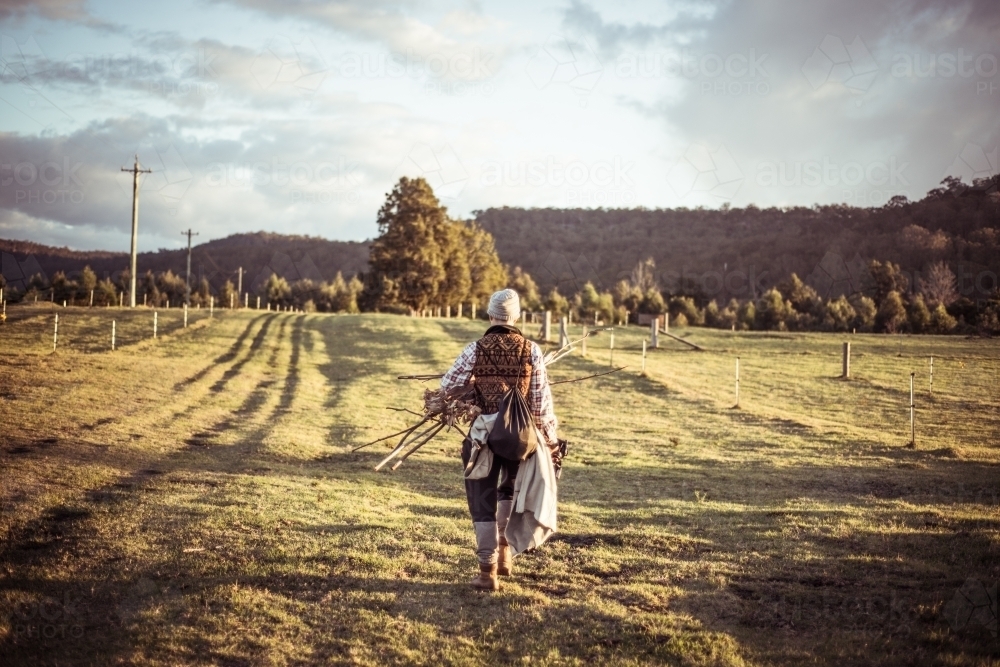 Person walking through paddock to campsite with kindling sticks for fire - Australian Stock Image
