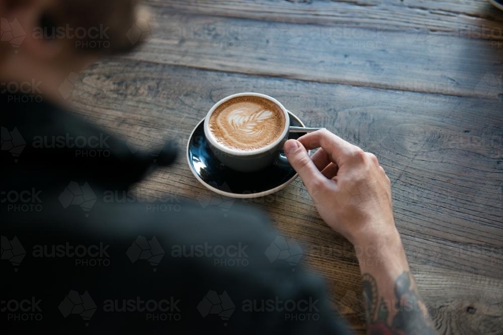 Person with a coffee on a wooden table - Australian Stock Image