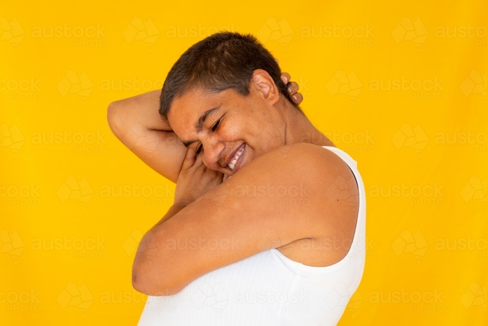 person with close-cropped hair and arms around head on yellow background - Australian Stock Image