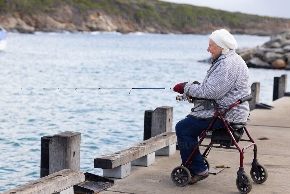 person with mobility issues sitting on wheeled walker while fishing off Bremer Bay jetty - Australian Stock Image