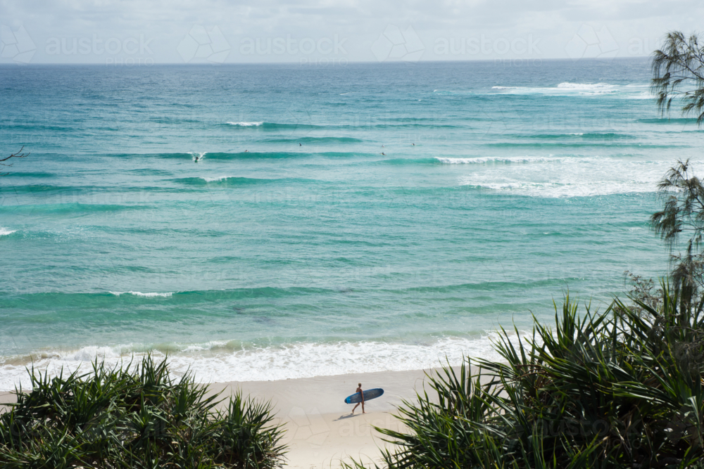 Person with surfboard on beach with ocean behind at Byron Bay - Australian Stock Image