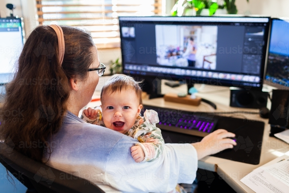 photographer mum working on computer in home office with young baby - Australian Stock Image