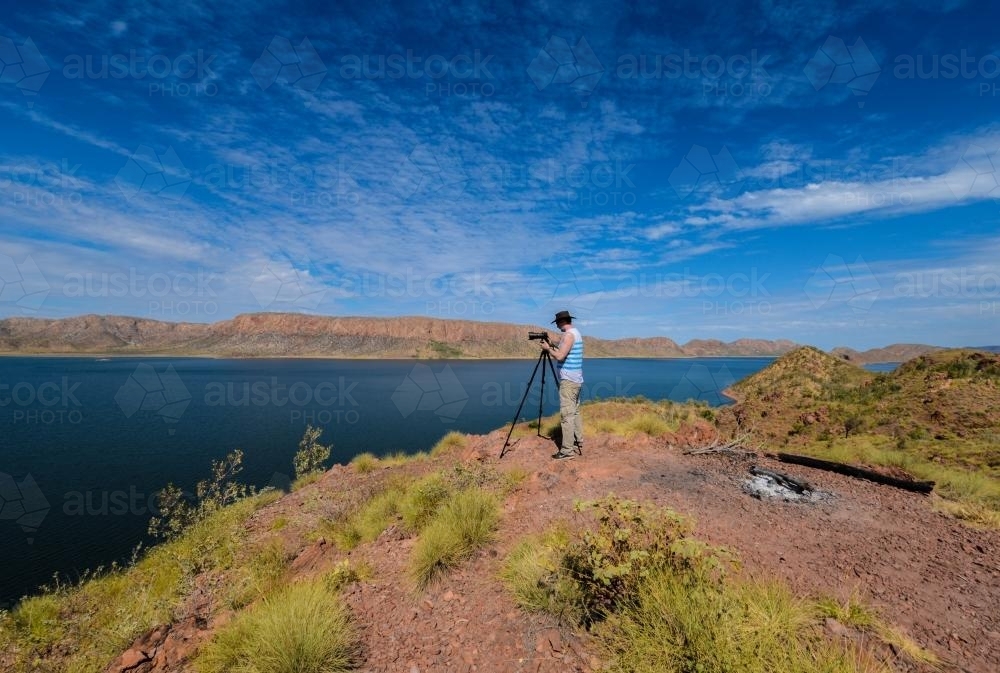 Photographer on cliff looking over a lake - Australian Stock Image