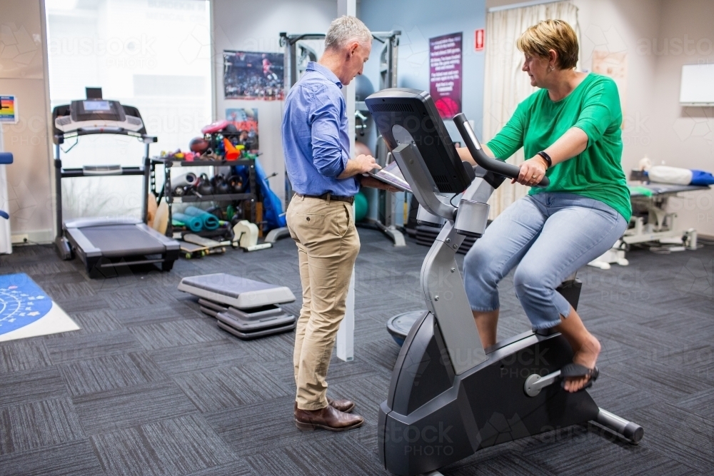 physio having consultation with woman client on exercise bike - Australian Stock Image