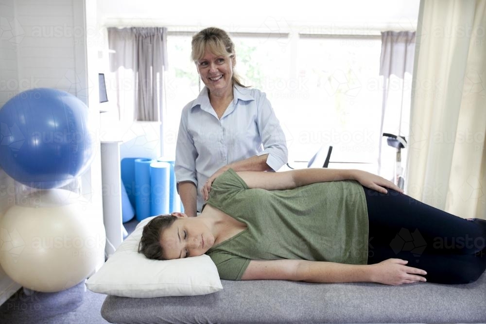 Physiotherapist treating a female patient lying on a bed - Australian Stock Image