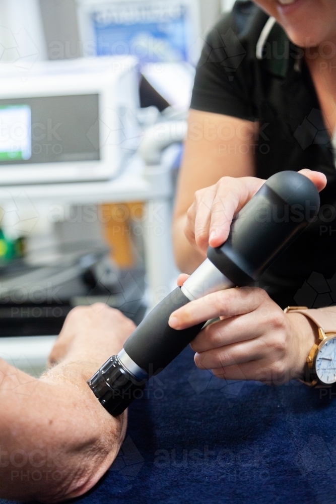 Image of Physiotherapist using shockwave therapy machine on clients arm