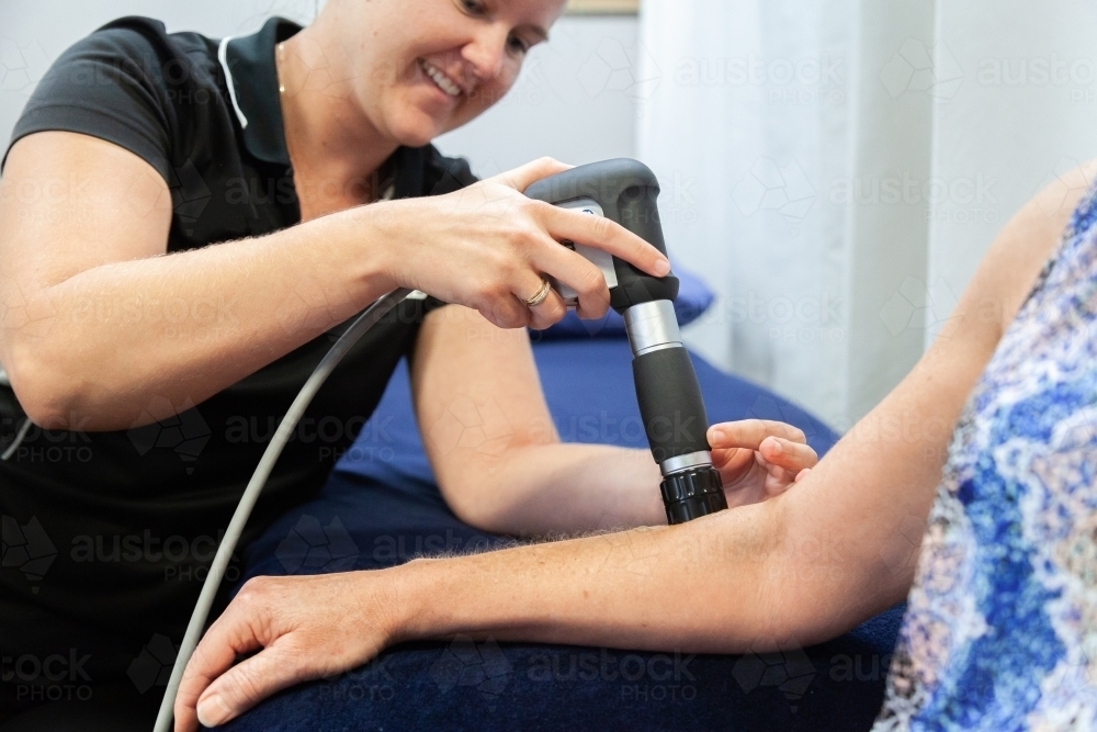 Physiotherapist using shockwave therapy machine on clients arm - Australian Stock Image