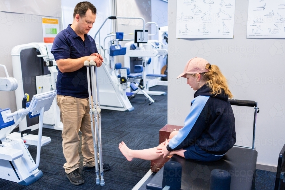 Physiotherapist working with teen girl teaching her how to use crutches  to walk with only one - Australian Stock Image