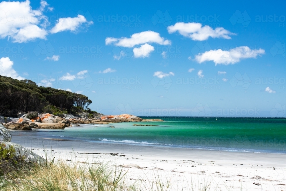 Picturescue white beach with orange rocky point, turquoise sea and blue sky with fluffy white clouds - Australian Stock Image