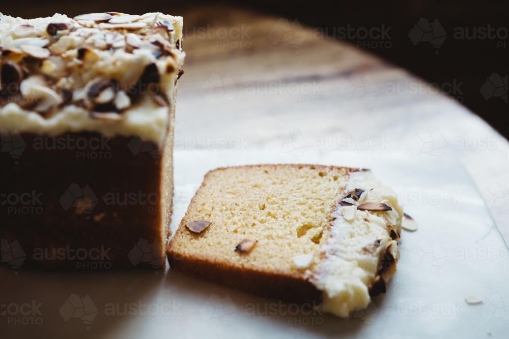 Piece of sliced almond cake on rustic wooden table and marble platter - Australian Stock Image