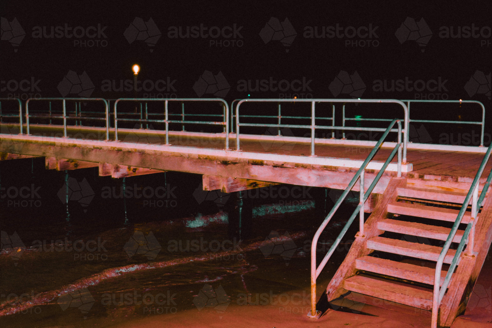 Pier glowing red with artificial light over dark coastal waters - Australian Stock Image