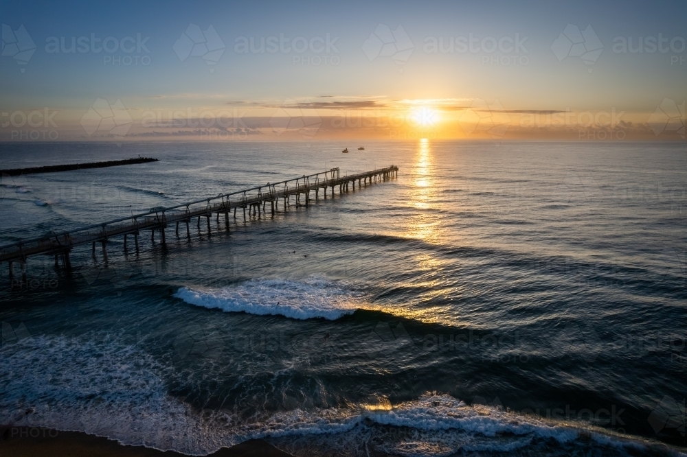 Pier going off in the distance with the sunrise over the ocean on a clear morning off the coast - Australian Stock Image