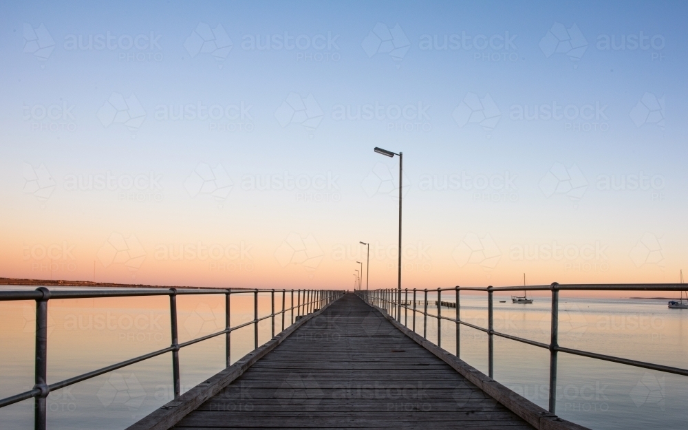 Pier leading out to the distance into the ocean on a clear dawn morning : Austockphoto Pier leading out to the distance into the ocean on a clear dawn morning - Australian Stock Image