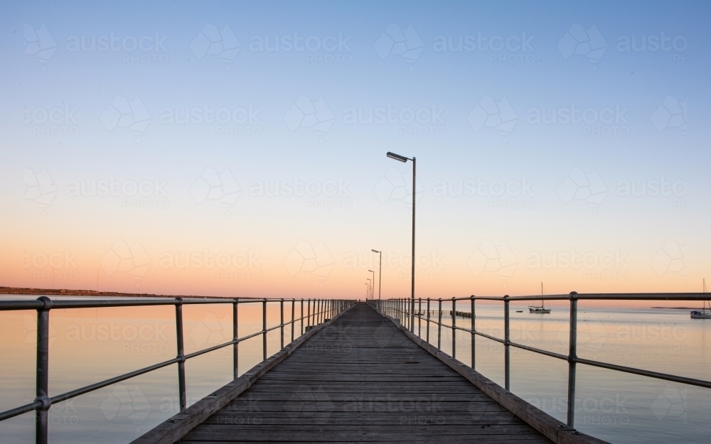 Pier leading out to the distance into the ocean on a clear dawn morning - Australian Stock Image