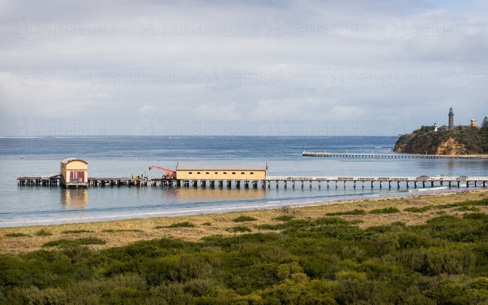 Pier with sheds and lighthouse in background - Australian Stock Image