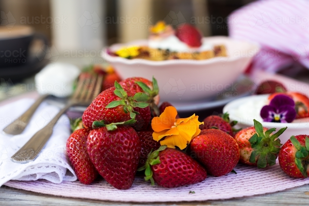 Pile of strawberries on a table with strawberry dessert in the background - Australian Stock Image
