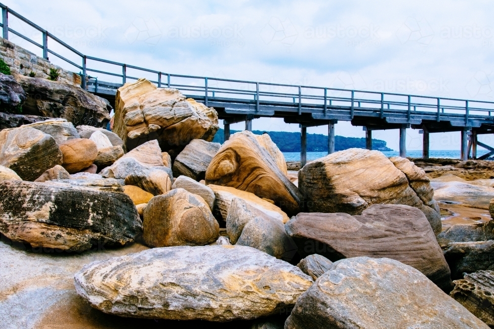 Piled up boulders and rocks with textures and bridge in the background - Australian Stock Image
