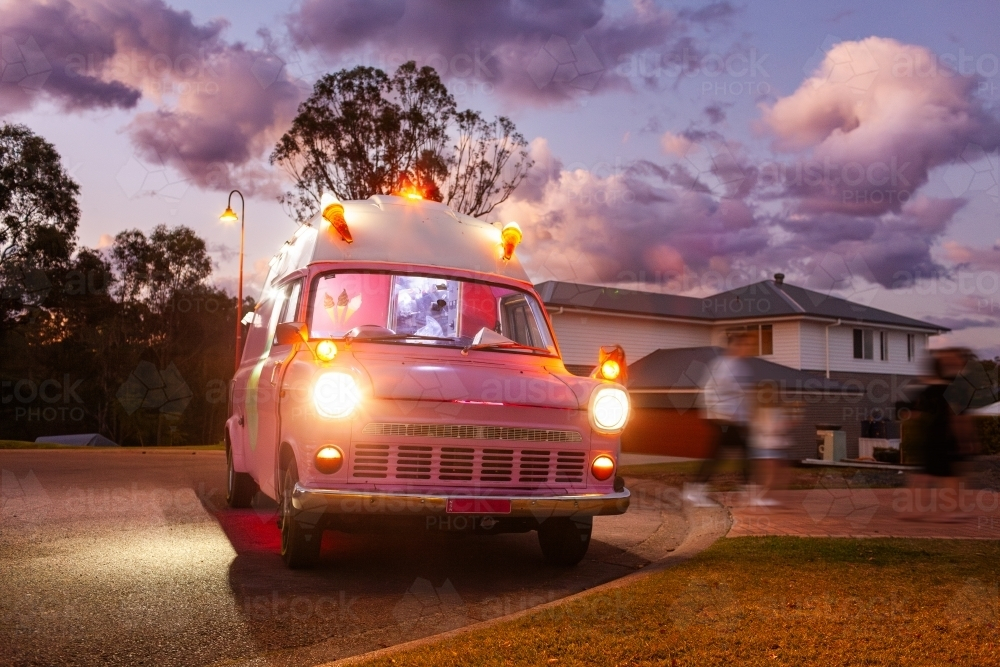 Pink Ice cream truck at dusk in suburban area with lights on selling ice-cream - Australian Stock Image