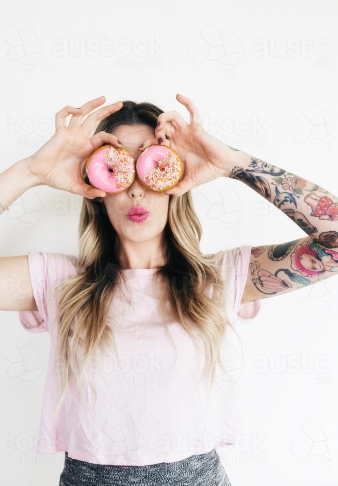 Pink iced donut eyes on blonde girl with tattoos - Australian Stock Image