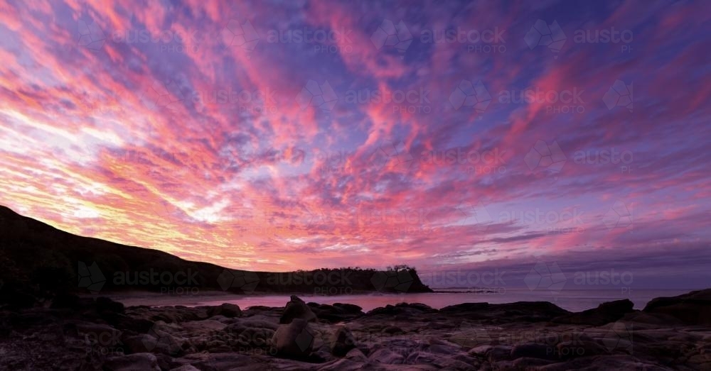 Pink, orange lines of clouds over beach at sunset - Australian Stock Image