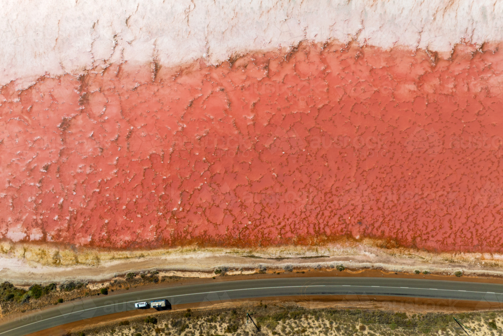 Pink salt lake meeting a lonely Outback road. - Australian Stock Image