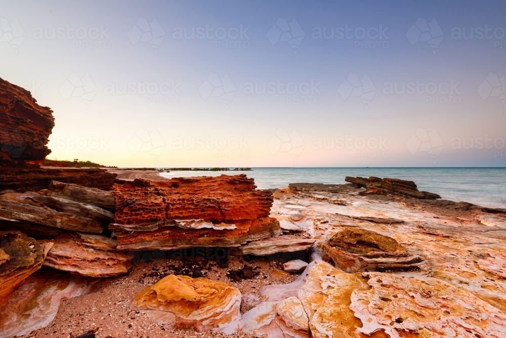 Pink sunset lighting on patterned rocky beach and bay - Australian Stock Image