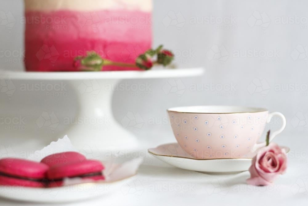 Pink tea cup beside macaron and cake - Australian Stock Image