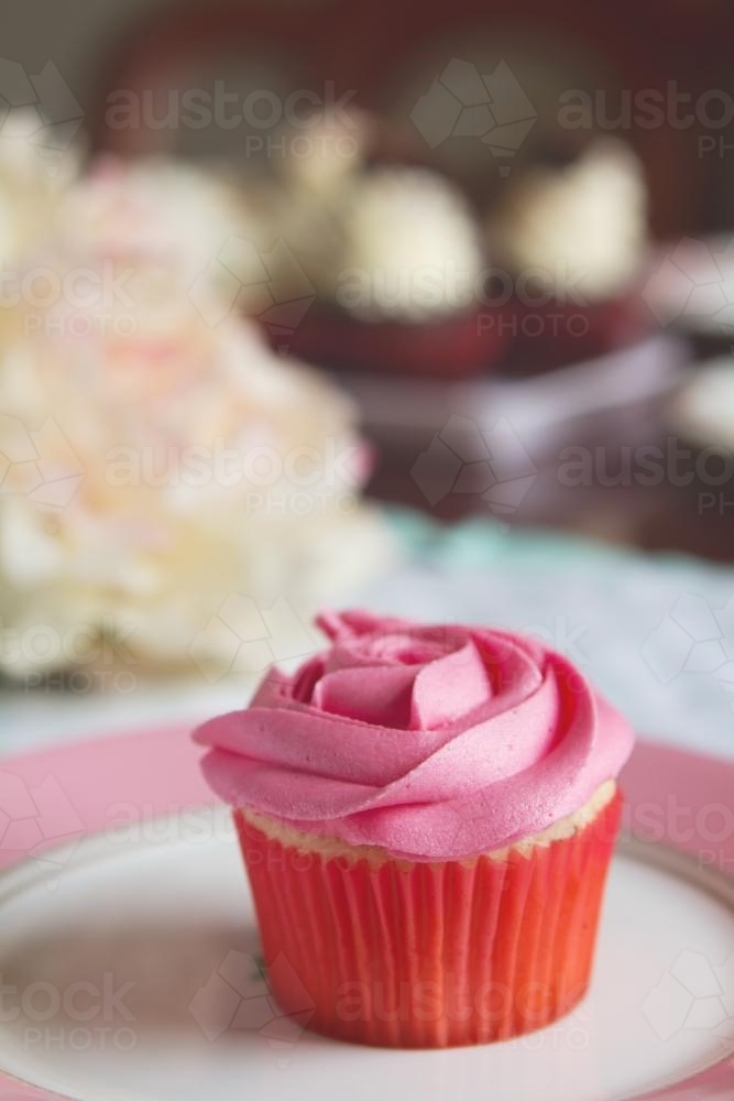 Pink vanilla rose cupcake with blurred cakes behind - Australian Stock Image