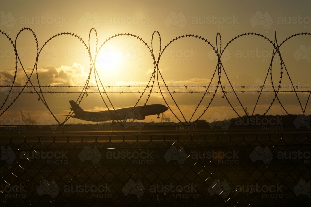 Plane landing at sunrise through security fence - Australian Stock Image