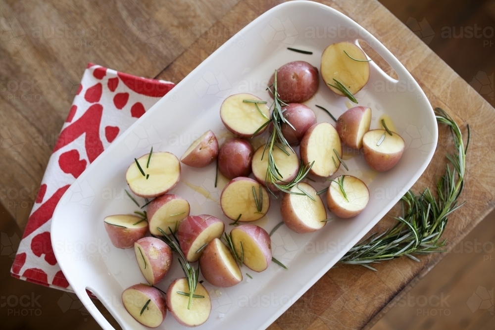 Plate of potatoes with rosemary sitting on wooden bench - Australian Stock Image