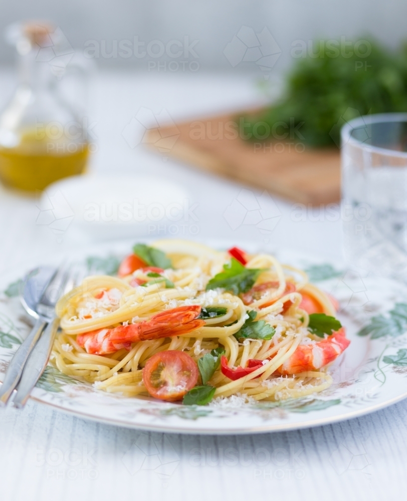 Plate with a serving of fresh prawn pasta, with green herbs and oil in the background - Australian Stock Image