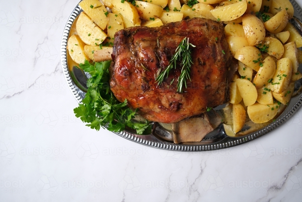 plate with roast meat and potatoes topped with fresh herbs - Australian Stock Image