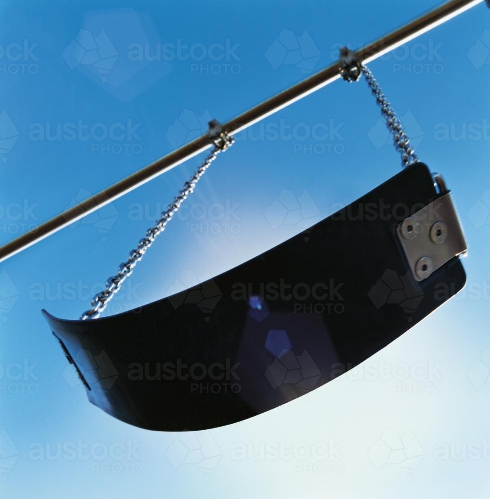 Playground swing from below with sun and blue sky behind - Australian Stock Image