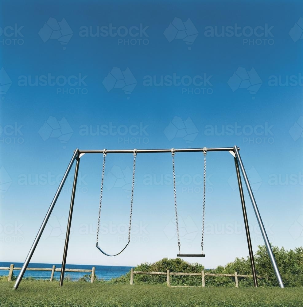 Playground swing set with blue sky and ocean background - Australian Stock Image