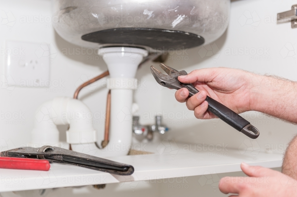 Plumber installing a sink and pipes with spanner - Australian Stock Image