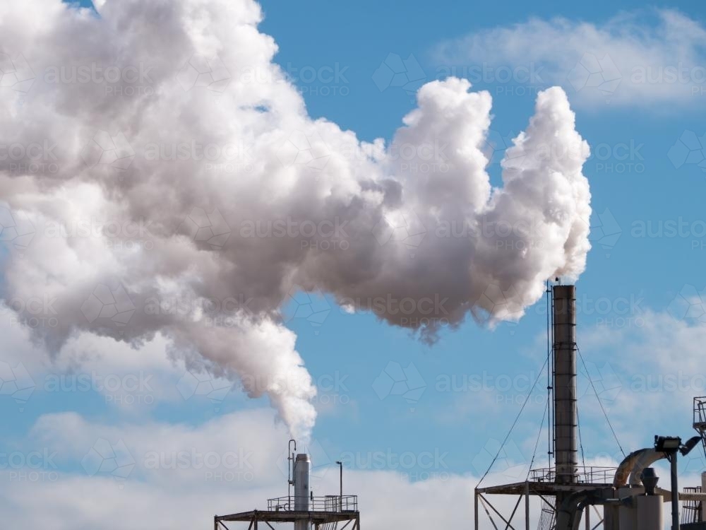 Plumes of steam rising from industrial chimneys into a blue sky - Australian Stock Image