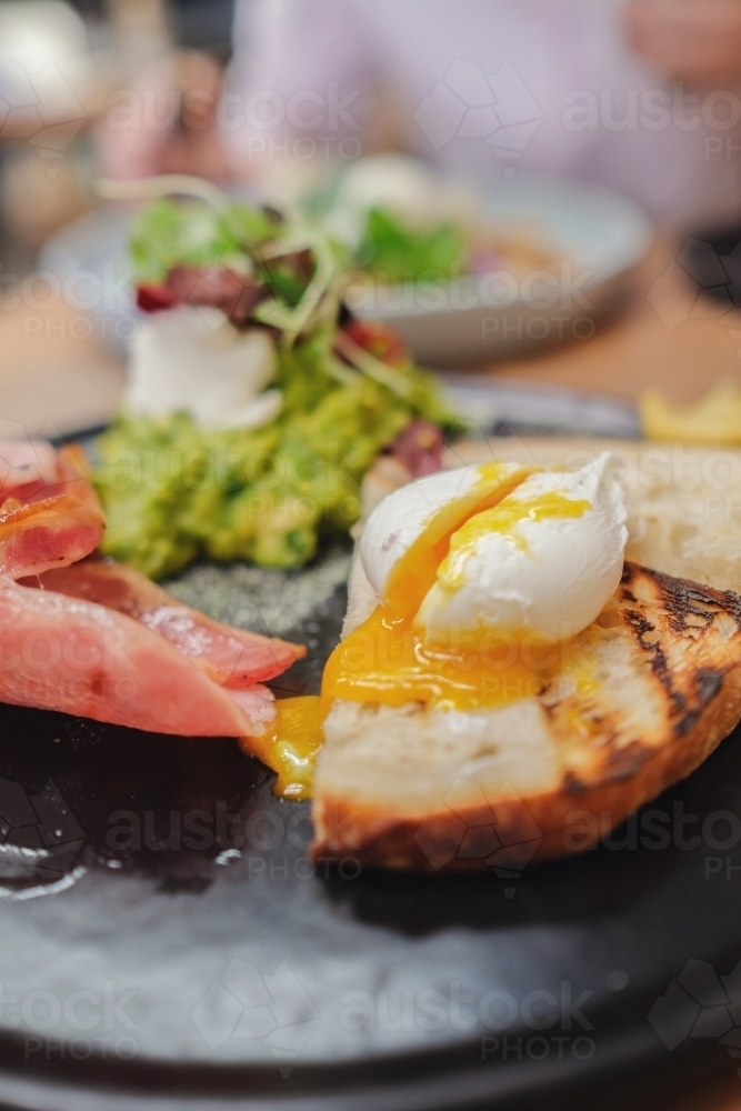 Poached egg on sourdough toast with bacon and mashed avocado - Australian Stock Image