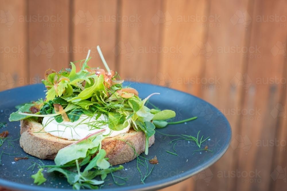 Poached egg on toast with goats curd and topped with green leaves and onion - Australian Stock Image
